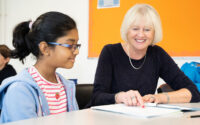 Smiling tutor going through a workbook with a girl in glasses.