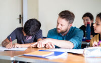 Tutor pointing to a boy's work as he helps him with a writing task.
