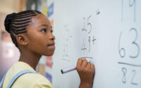 Girl working out an addition sum on a classroom whiteboard.
